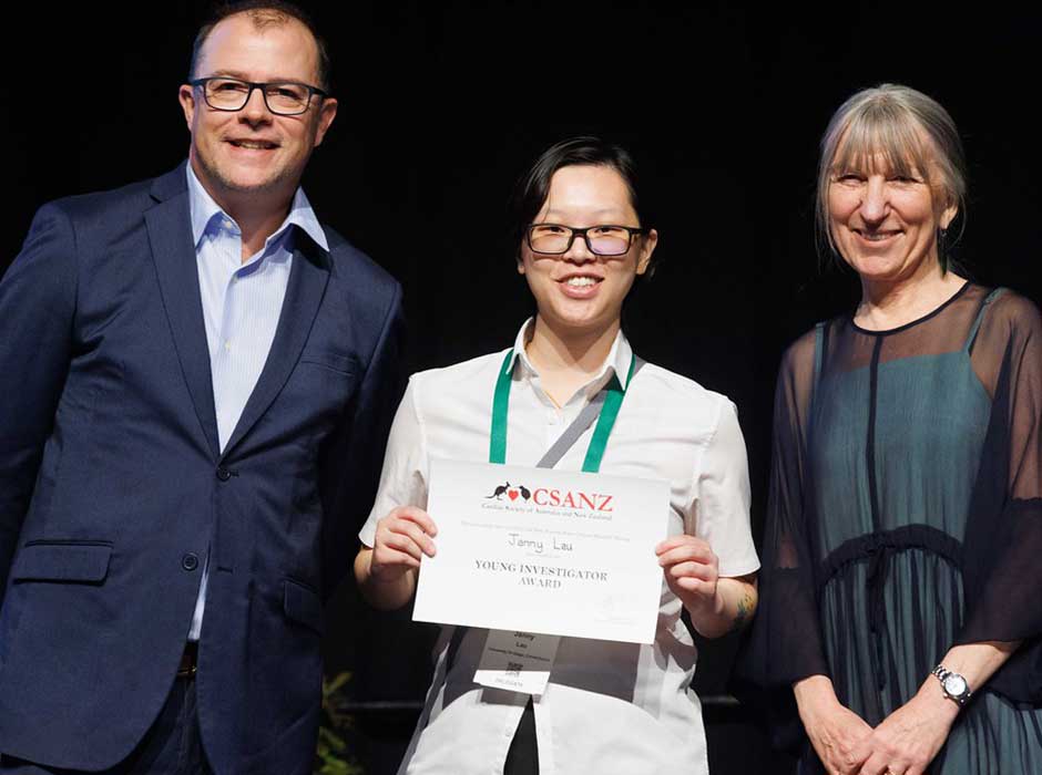 Three people standing smiling one in the centre holding an award 