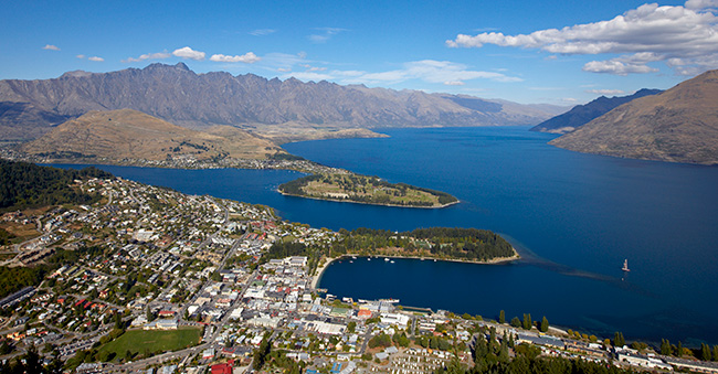 Aerial view of a town on the edge of a large, blue lake surrounded by mountains.