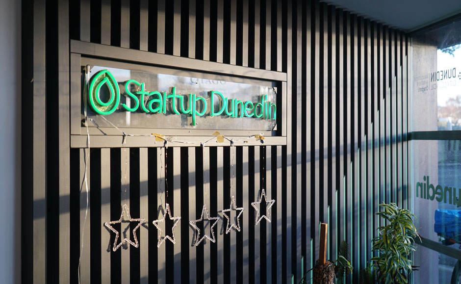 Flurescent light sign reading 'Startup Dunedin' on a wall inside a lobby.