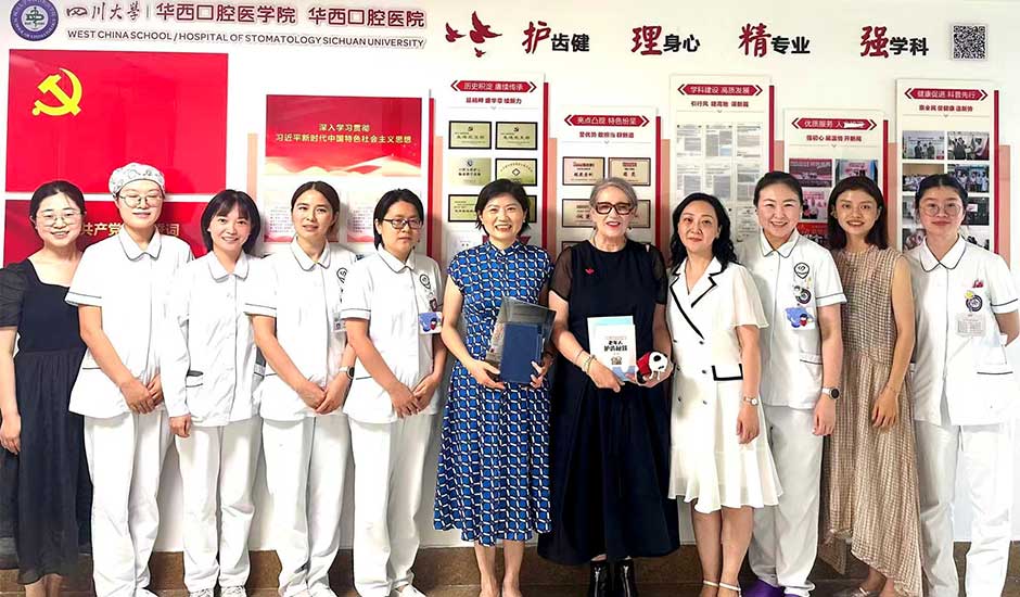 A row of stand, some in white nurses uniforms, smiling, in front of a  wall with Chinese scripture on it