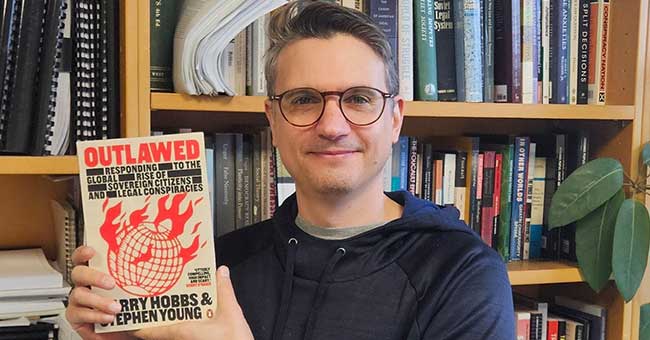 A man standing in front of a bookcase holding a book