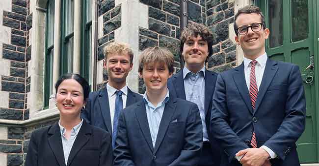 Five people standing in suits next to each other on stairs 