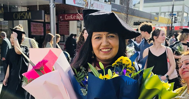 A woman in graduation gear holds flowers at the graduation procession.