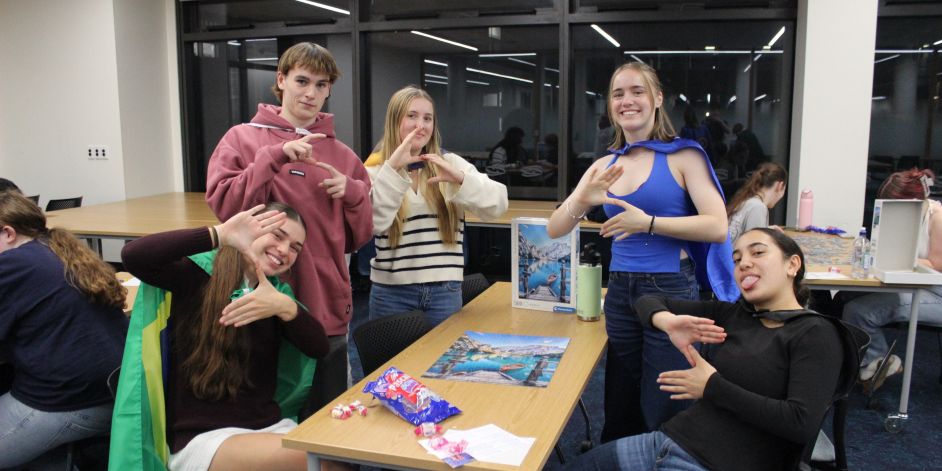 Five students proudly standing by a completed jigsaw puzzle.