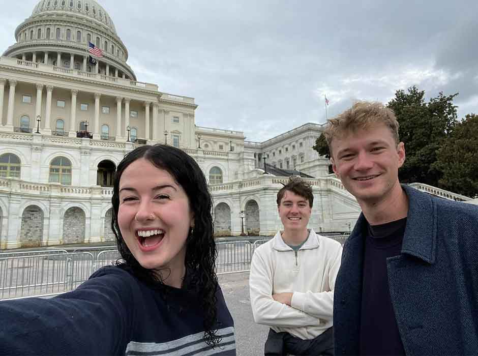three people take a selfied together in front of the United States Capitol building