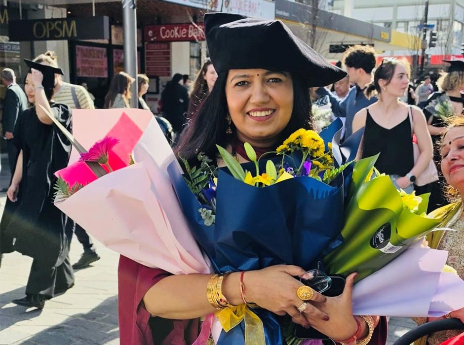 A woman in graduation gear holds flowers at the graduation procession.
