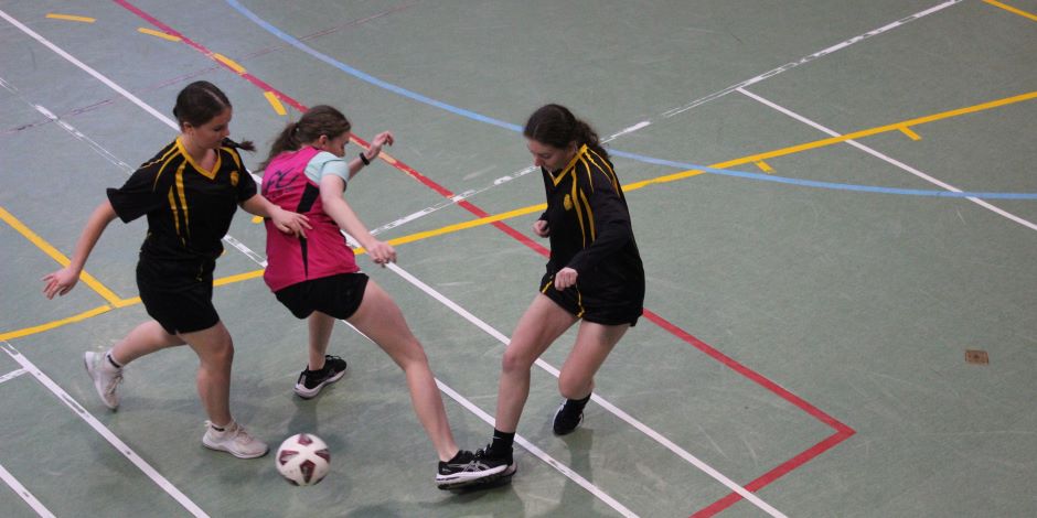 A view from above of three students engaged in a futsal tackle