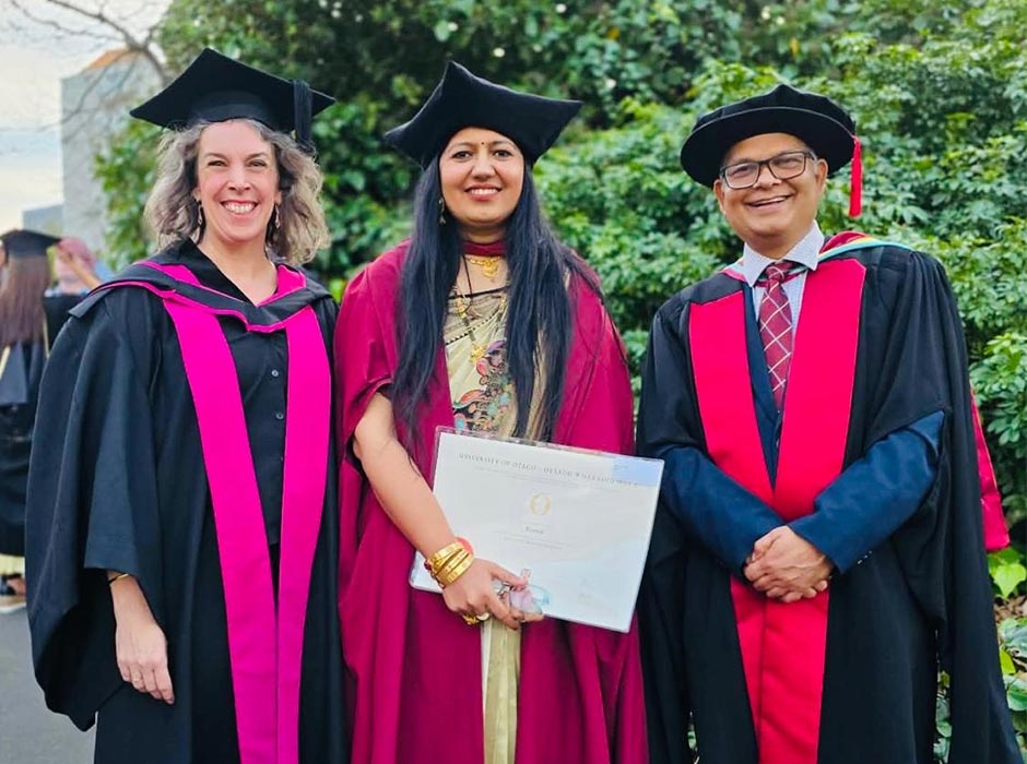 Three people in academic robes pose at graduation.