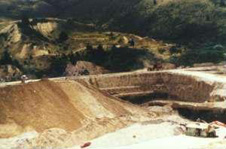 Nokomai alluvial gold mine, south of Queenstown (now closed and rehabilitated) had a 40 metre high gravel wall around the workings. The bottom 2 metres contained profitable gold, which was extracted on the floating plant (lower right). The plant was fed by a large digger whose bucket reached below water level to the gravel sitting on the schist bedrock.