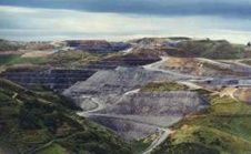 
Macraes hard-rock gold mine showing the main features of a large scale open pit. The excavated pit is on the left (each bench is 10 metres high). Waste rock from the pit is piled on the skyline, with older piles grassed over. The processing plant is centre right, and tailings from this plant are discharged as a slurry into a large dam (far right and beyond this view).