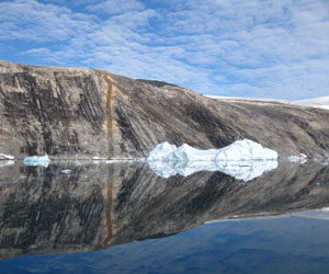 Cliff face reflected in the mirror calm water of De Dødes Fjord, NW Greenland