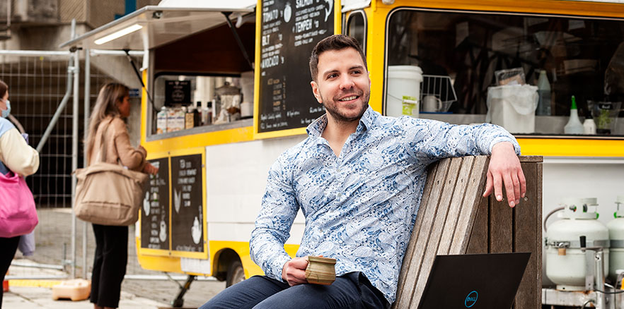 Daniel Alencar da Costa sitting on a bench outside next to a coffee truck