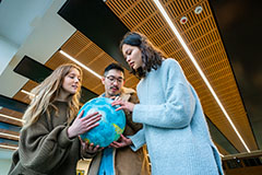 Three students holding andf looking at a globe