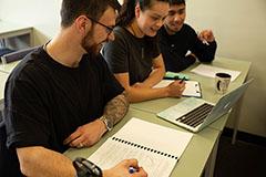 Three students sitting at desk and taking notes
