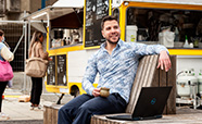 Daniel Alencar da Costa sitting on a bench outside next to a coffee truck
