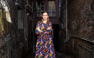 Anna High standing in an alley wearing a brightly coloured dress