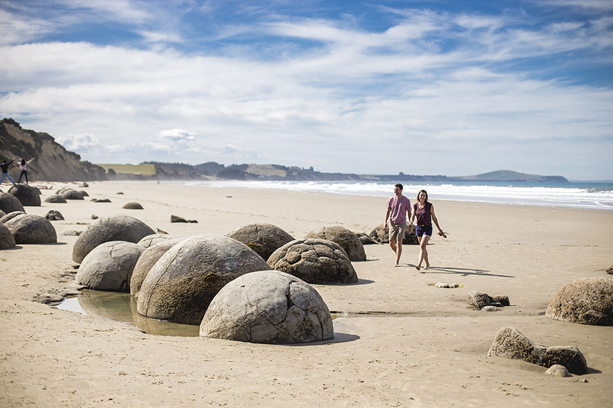 Two people walking barefoot by the Moeraki boulders