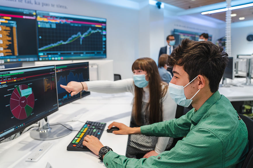 Two students wearing masks using computers in the <abbr>BNZ</abbr> Bloomberg Markets Lab