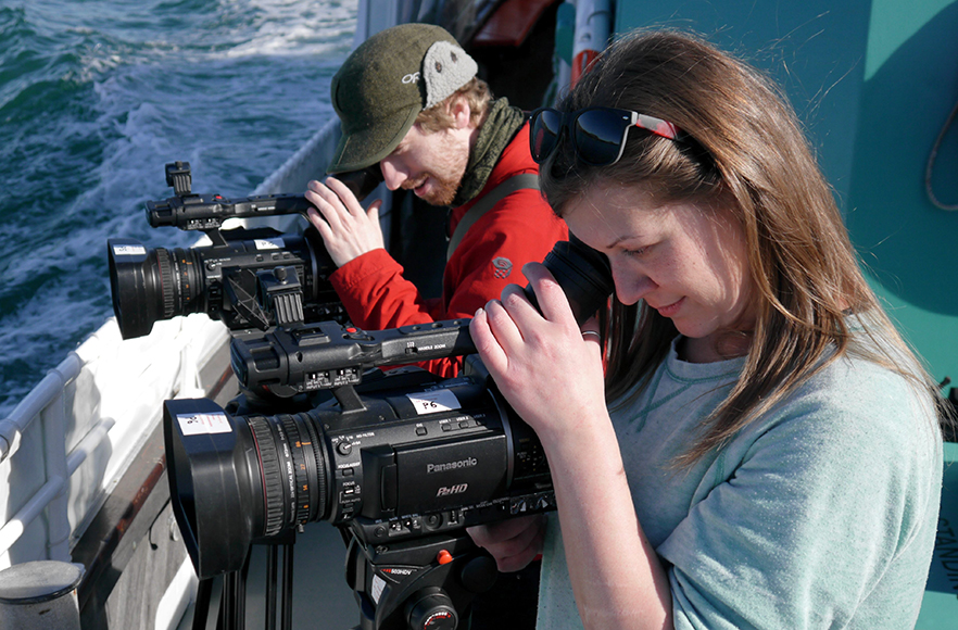 A man and woman filming with from two cameras on a boat at sea.