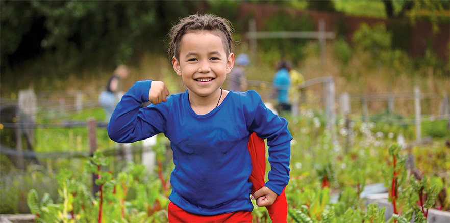 Child in superhero cape at a community garden