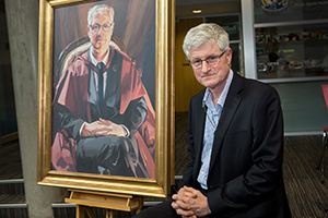 Peter Crampton sitting next to the portrait. 