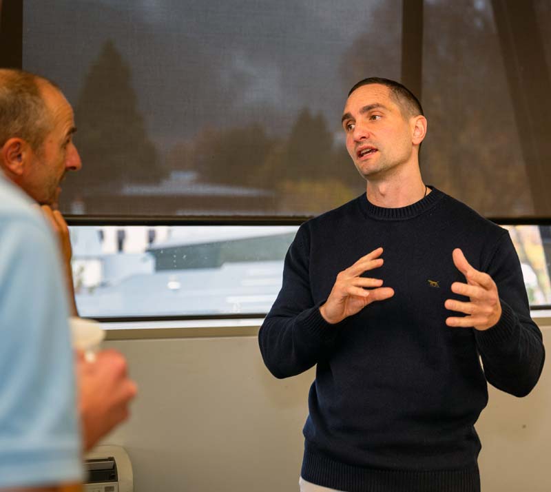 Two professionals in discussion at a table in a modern office setting overlooking Queenstown